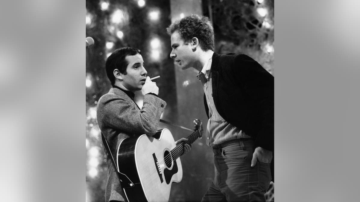Paul Simon holding a guitar while Art Garfunkel stands over him