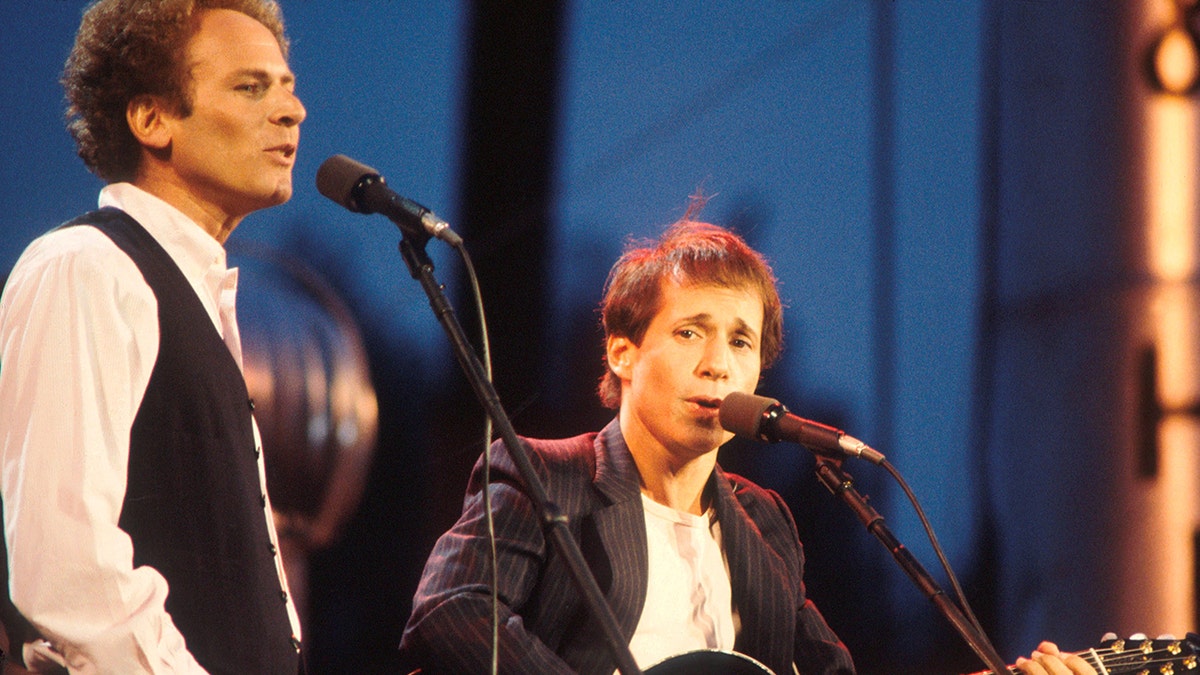 Art Garfunkel and Paul Simon singing into microphones on stage at Central Park