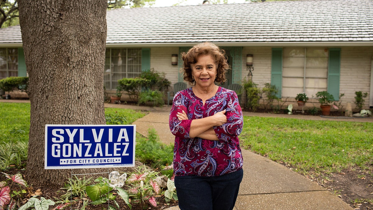 Sylvia Gonzalez está ao lado de sua placa de campanha em frente à sua casa