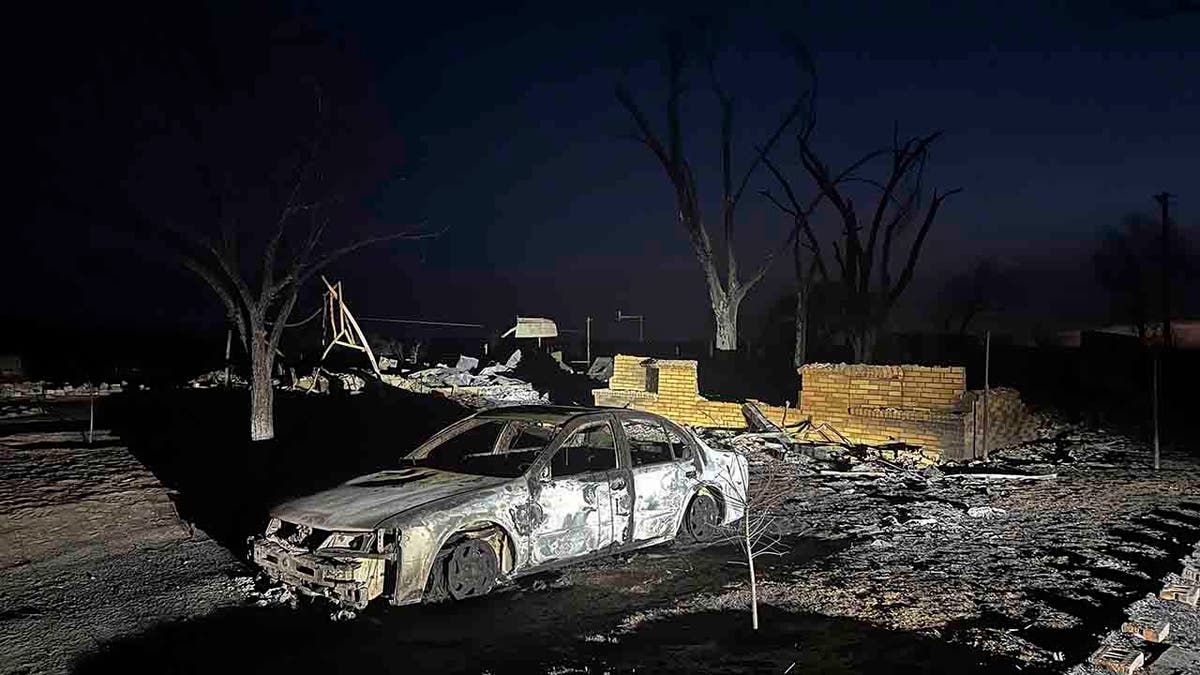 charred vehicle sits near the ruins of a home