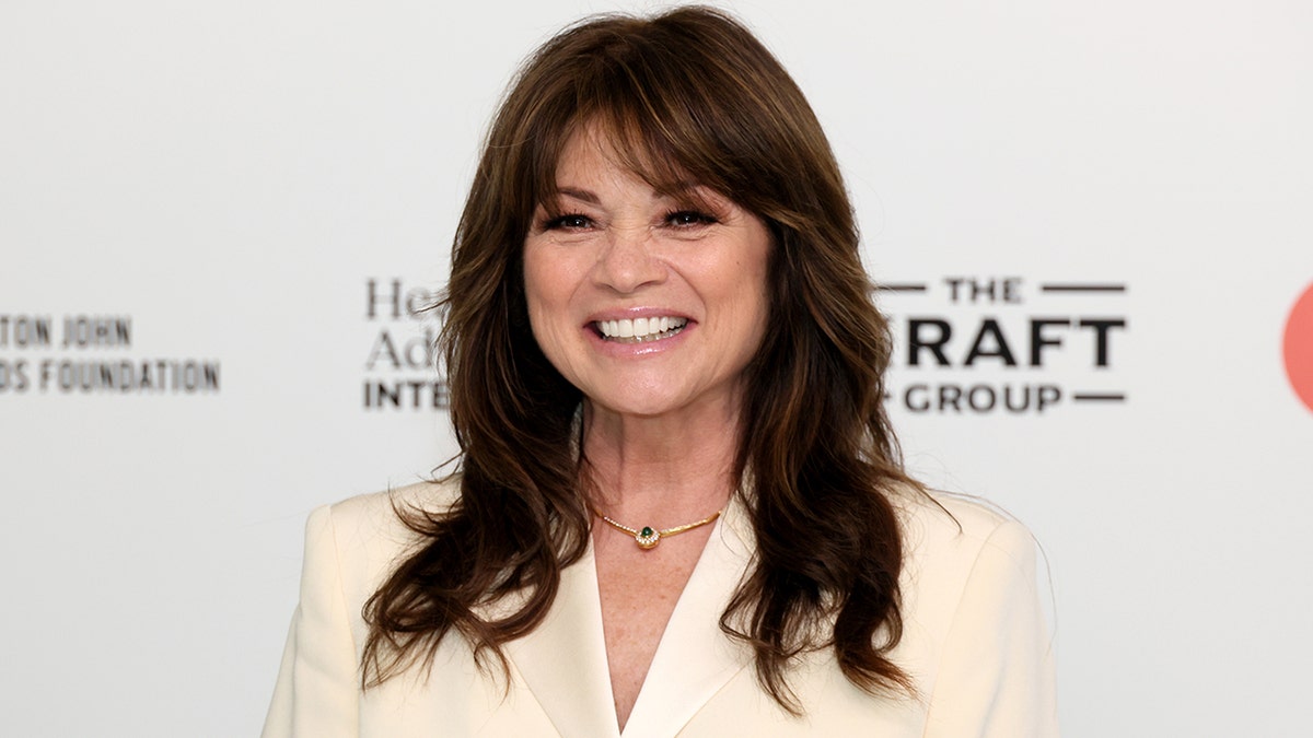 Valerie Bertinelli sorrindo em um terno creme com fundo branco