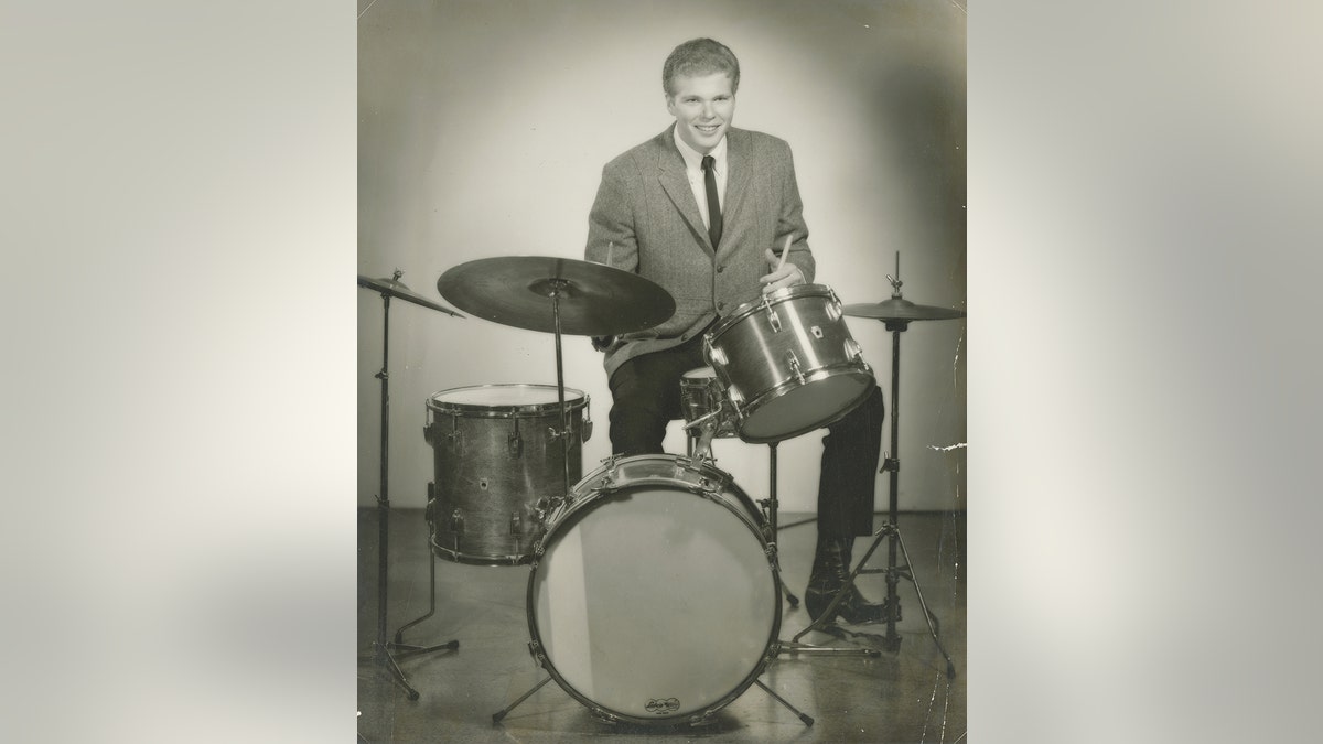 Um jovem Jim Gordon de terno tocando bateria