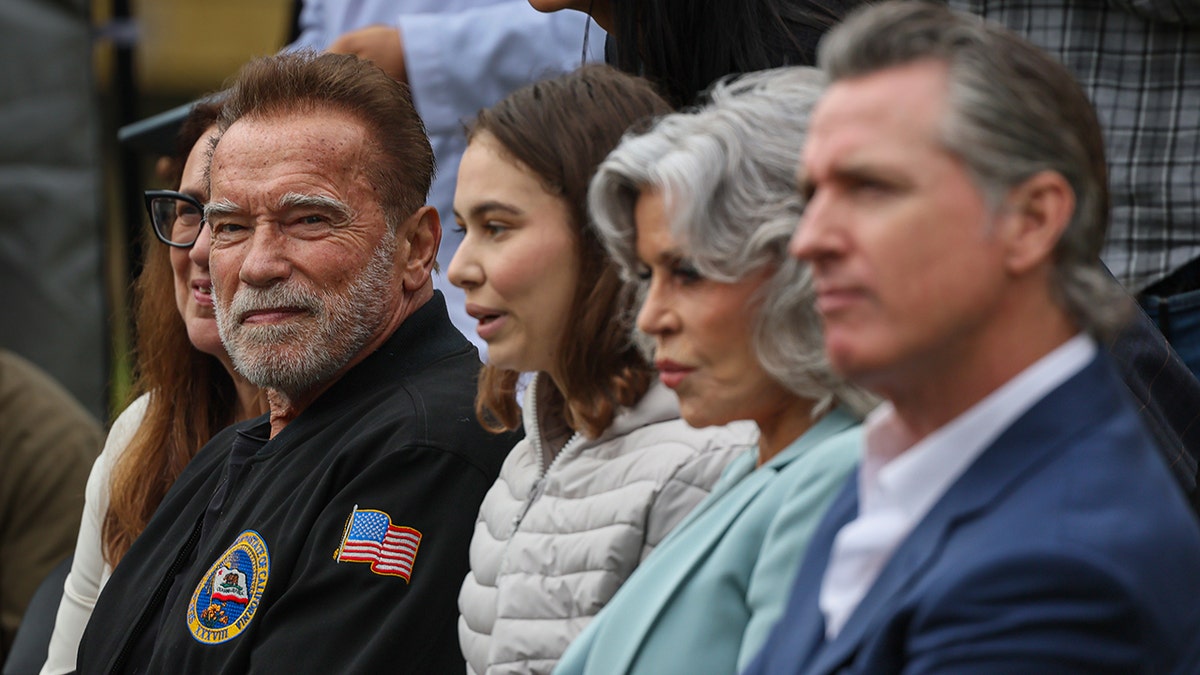 Arnold Schwarzenegger em foco senta ao lado de uma mulher, depois Jane Fonda e o governador Gavin Newsom em um evento ambiental em Los Angeles