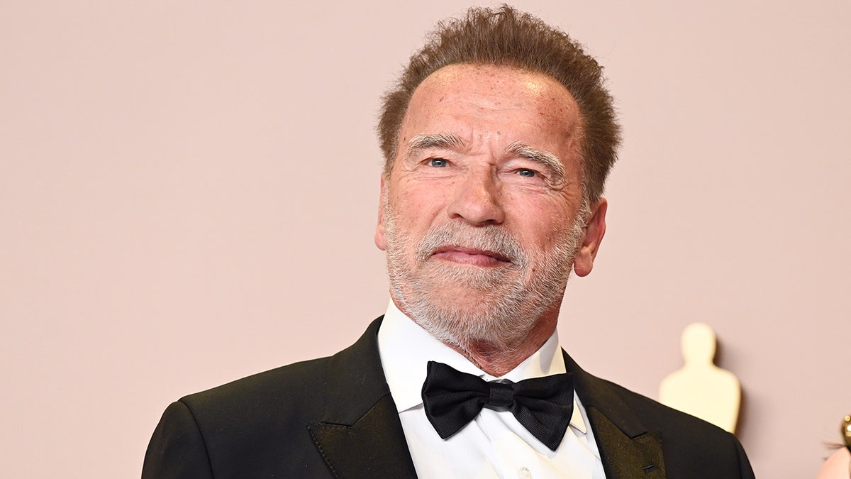 Arnold Schwarzenegger in a black tuxedo soft smiles on the Oscars carpet