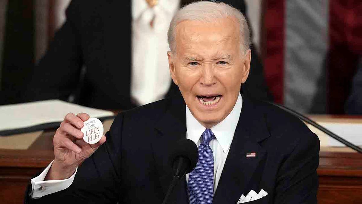 President Joe Biden holds up a Laken Riley button