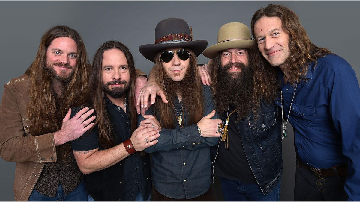 Brandon Still in a brown jacket stands next to Paul Jackson in a navy shirt and black vest, next to Charlie Starr with sunglasses and a big hat and Brit Turner with a big hat, and Richard Turner in a blue shirt