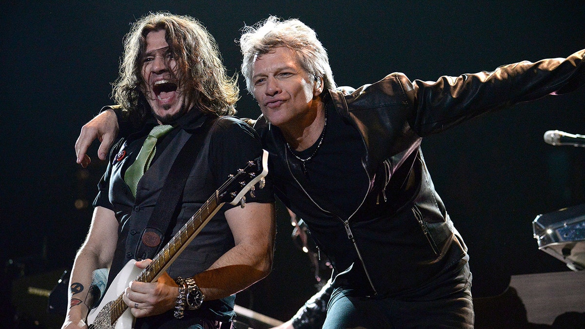 Phil X looks like he's yelling on stage playing the guitar as Jon Bon Jovi leans into him on stage