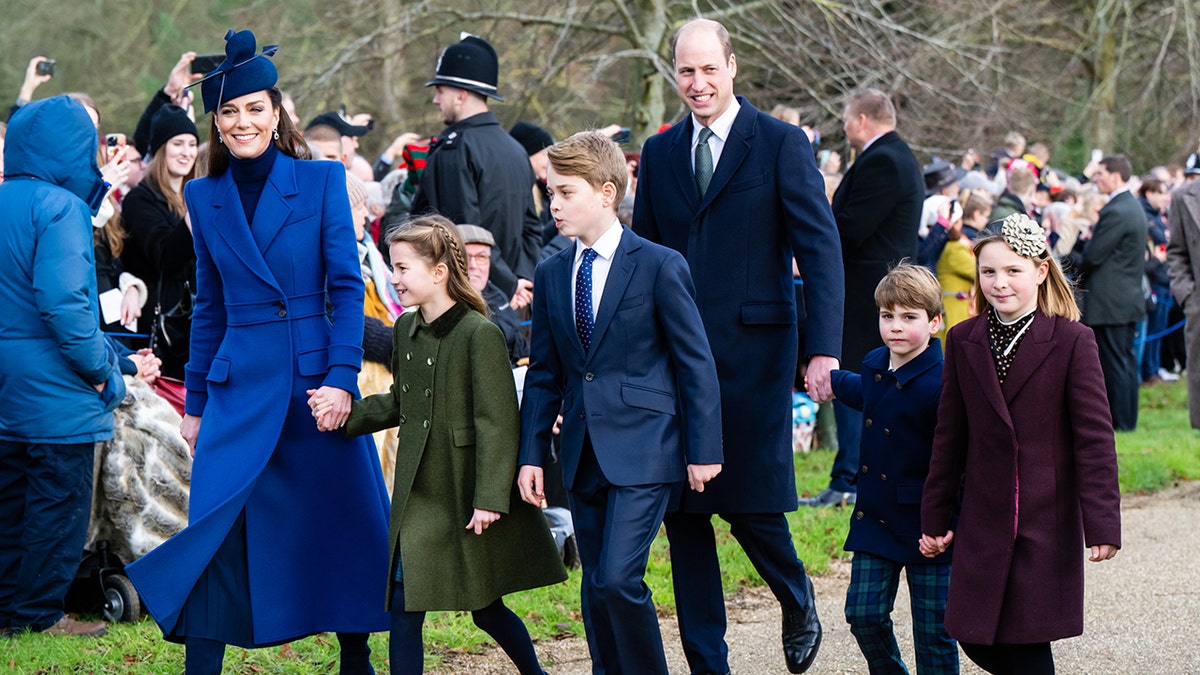 Princess Catherine in a royal blue jacket and hat holds Princess Charlotte's hand as she walks alongside Prince William, Prince George and Louis and Mia Tindall to Christmas service