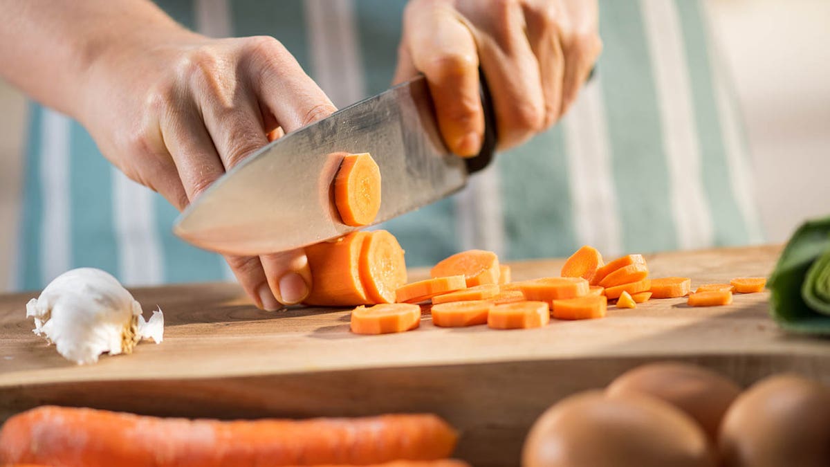 Close de uma pessoa cortando cenouras 