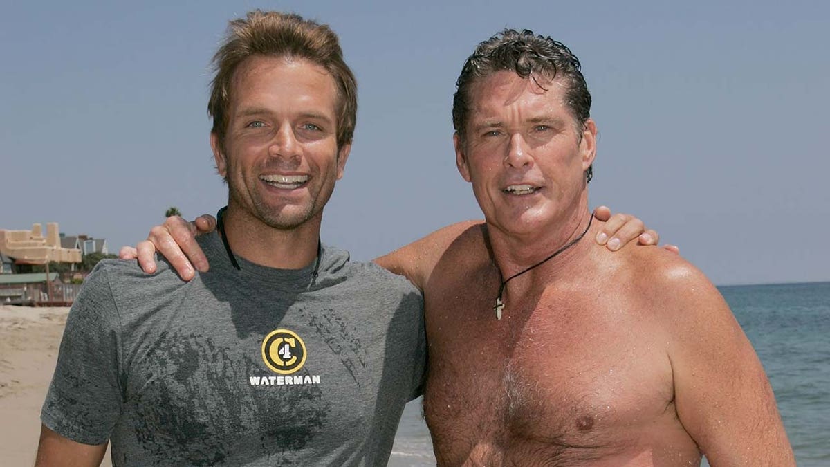 Baywatch stars David Chokachi and David Hasselhoff wrap their arms around each other on the beach.
