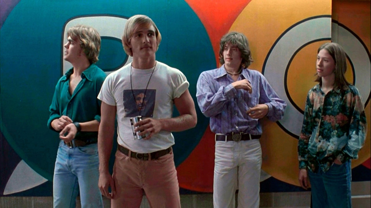 Matthew McConaughey in a white t-shirt and peach colored pants in a scene from "Dazed and Confused" stands around with other guys