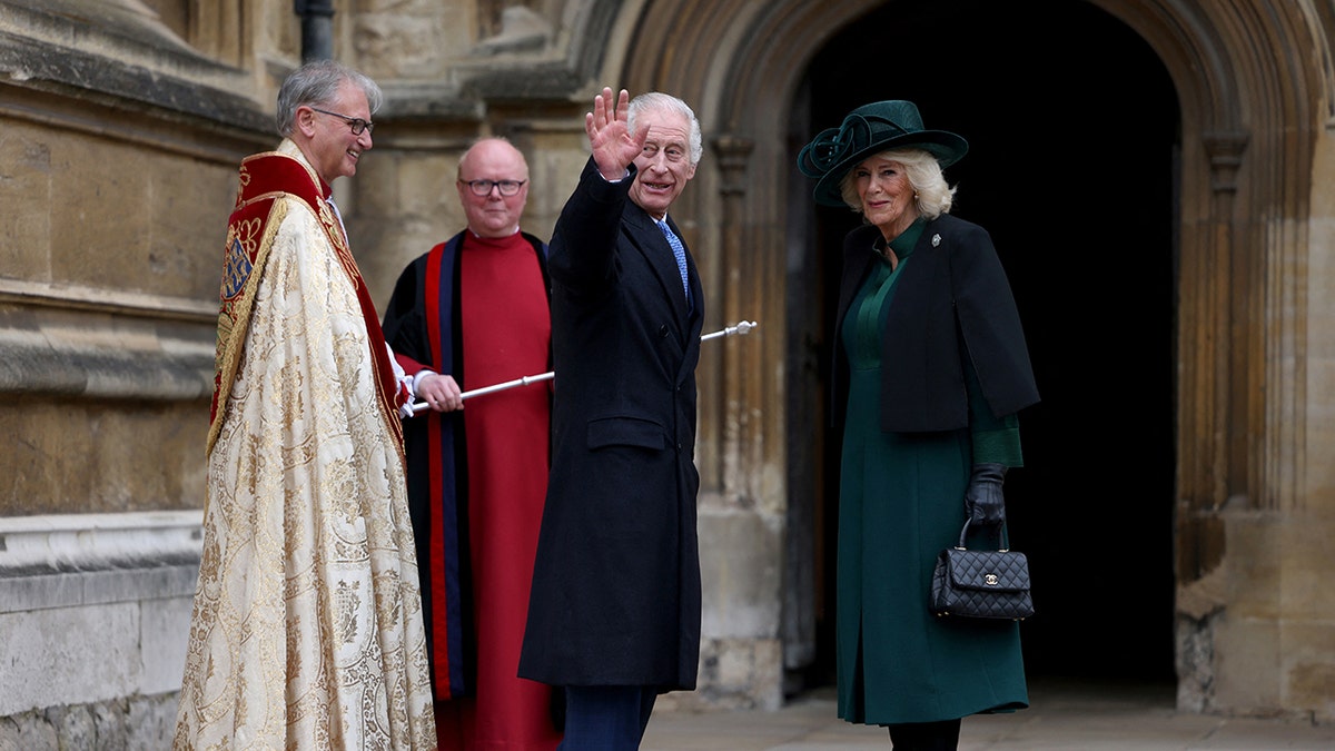 King Charles turns back and waves to spectators next to Queen Camilla and members of the clergy