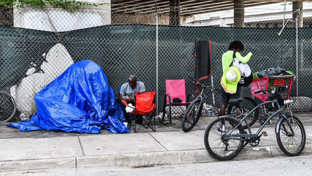 A homeless man sits next to his makeshift shelter on a sidewalk in Miami