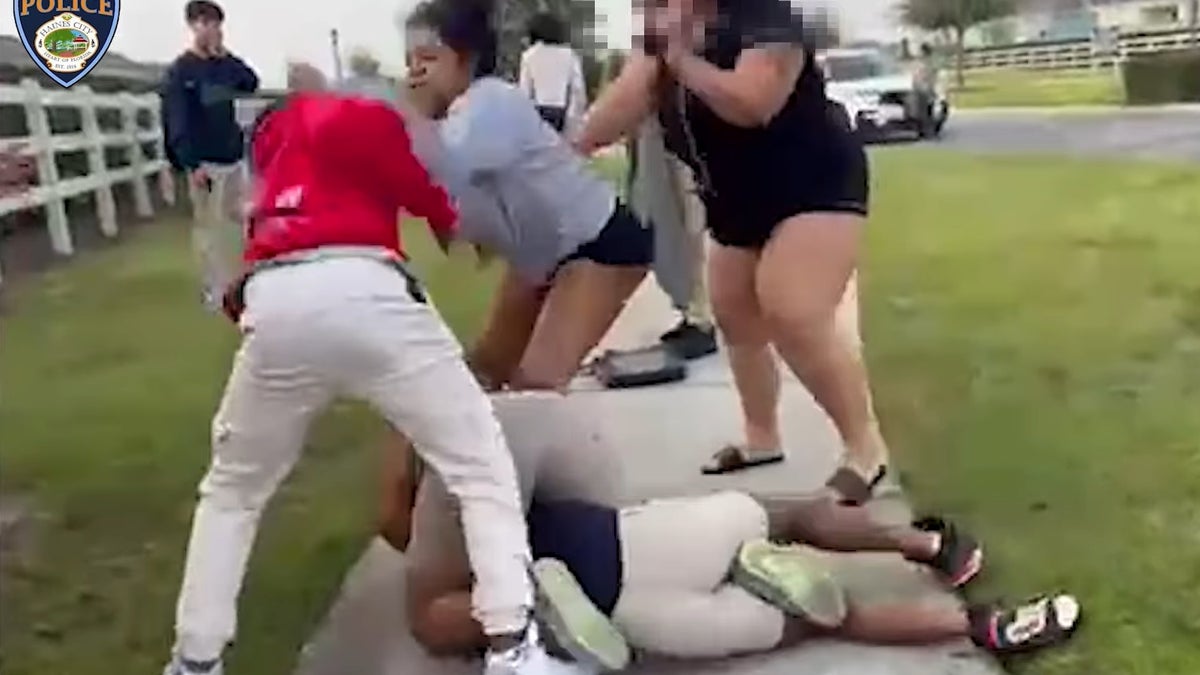Taitayana Duffy (gray sweatshirt and black shorts) was identified by police as one of the student's guardians and is seen here grabbing one of the students (in a red hoodie).