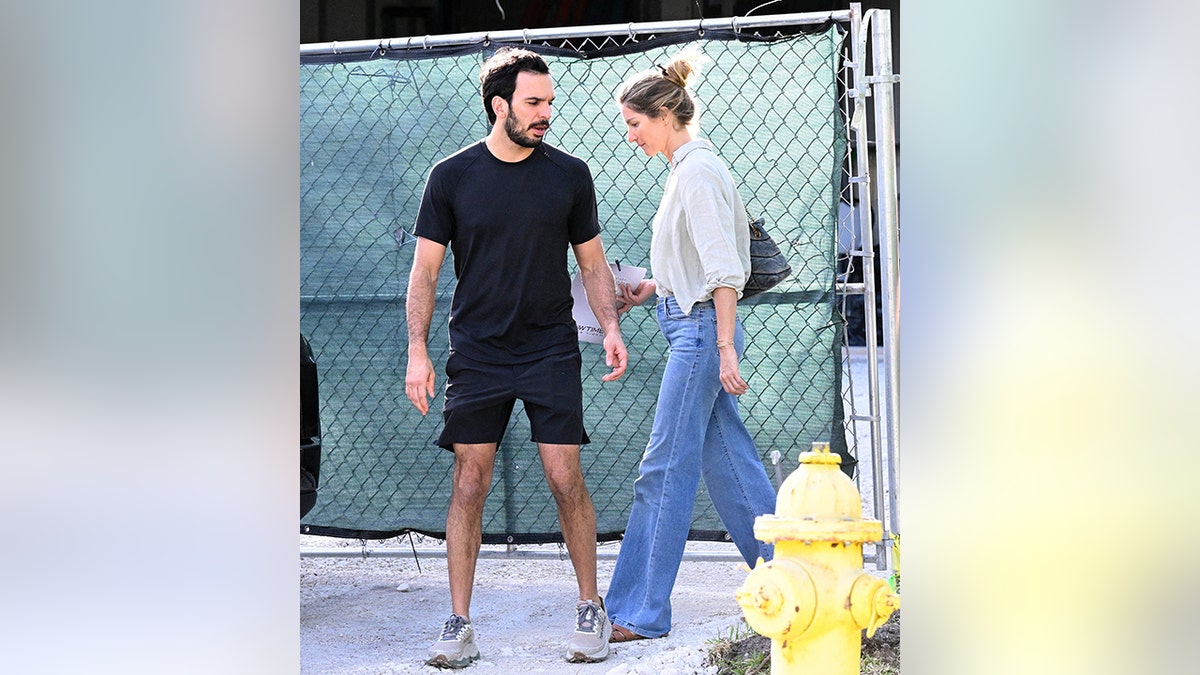 Joaquim Valente in a black shirt and shorts stands outside Gisele Bündchen's home as she walks behind him in jeans