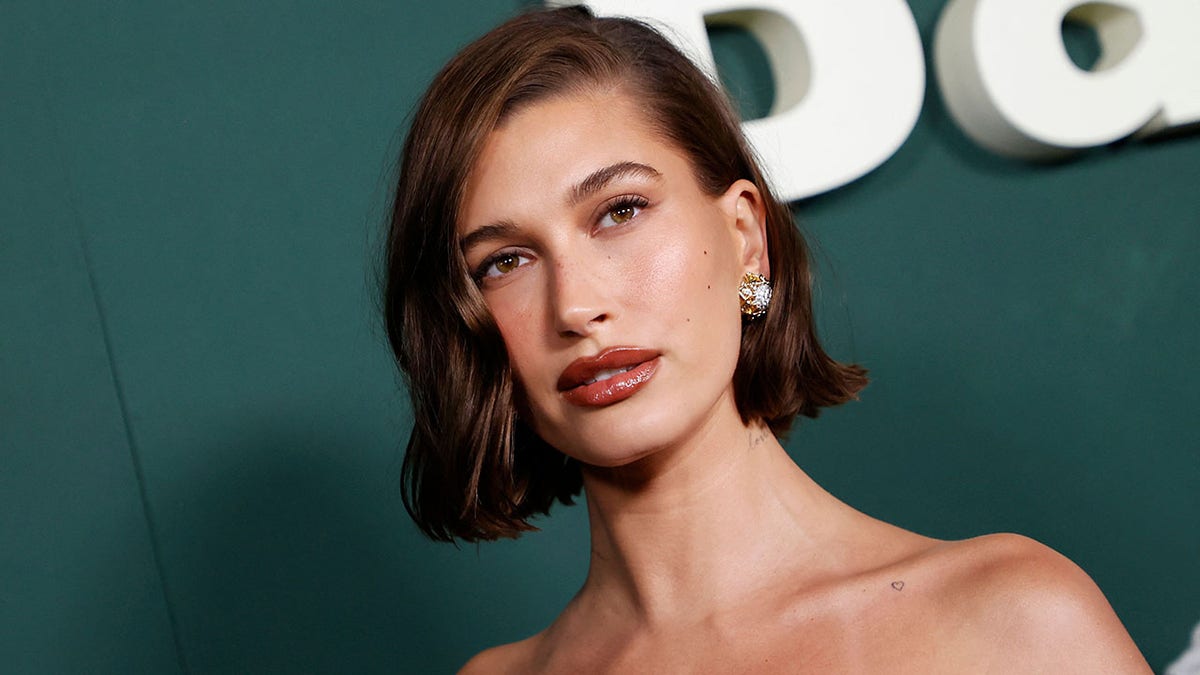 Hailey Bieber with a short brunette bob looks up on the red carpet in a strapless gown