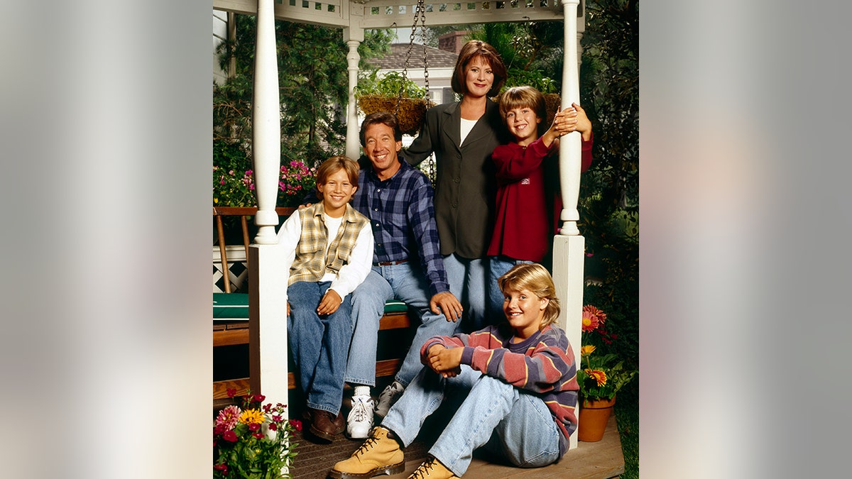 O elenco de "Melhoria da casa" sentado em um banco pendurado em pilares fora de casa
