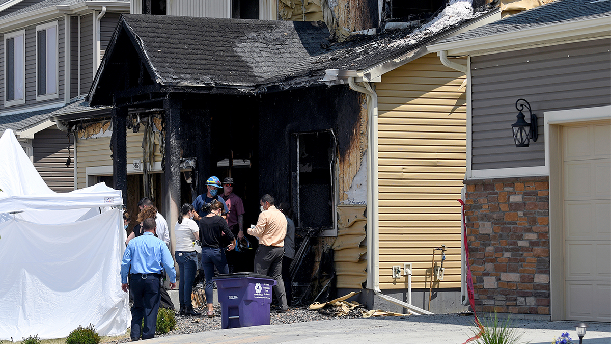 Investigators stand outside a house where five people were killed in a fire