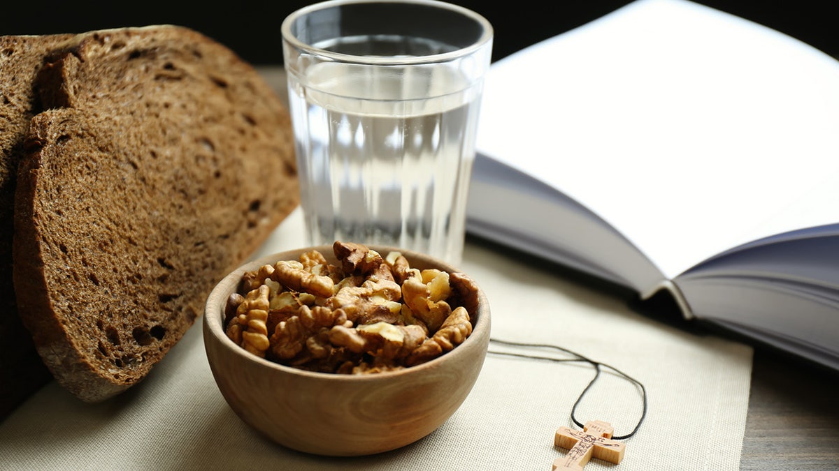 Bread, walnuts, water, Bible and crucifix on table.