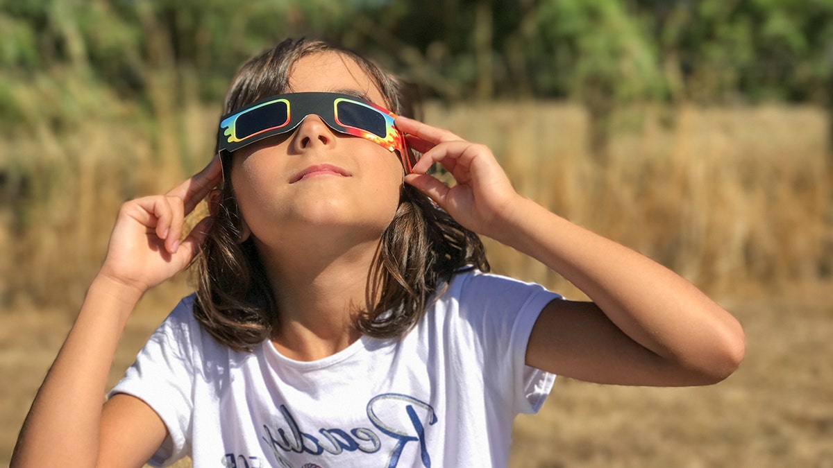 young girl looks at solar eclipse through glasses