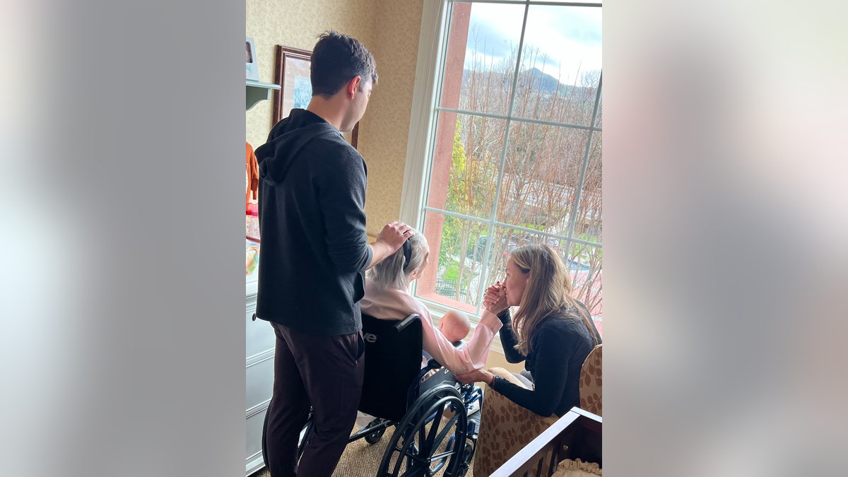 Barbara Rush com a filha e o neto, olhando pela janela sentada em uma cadeira de rodas.