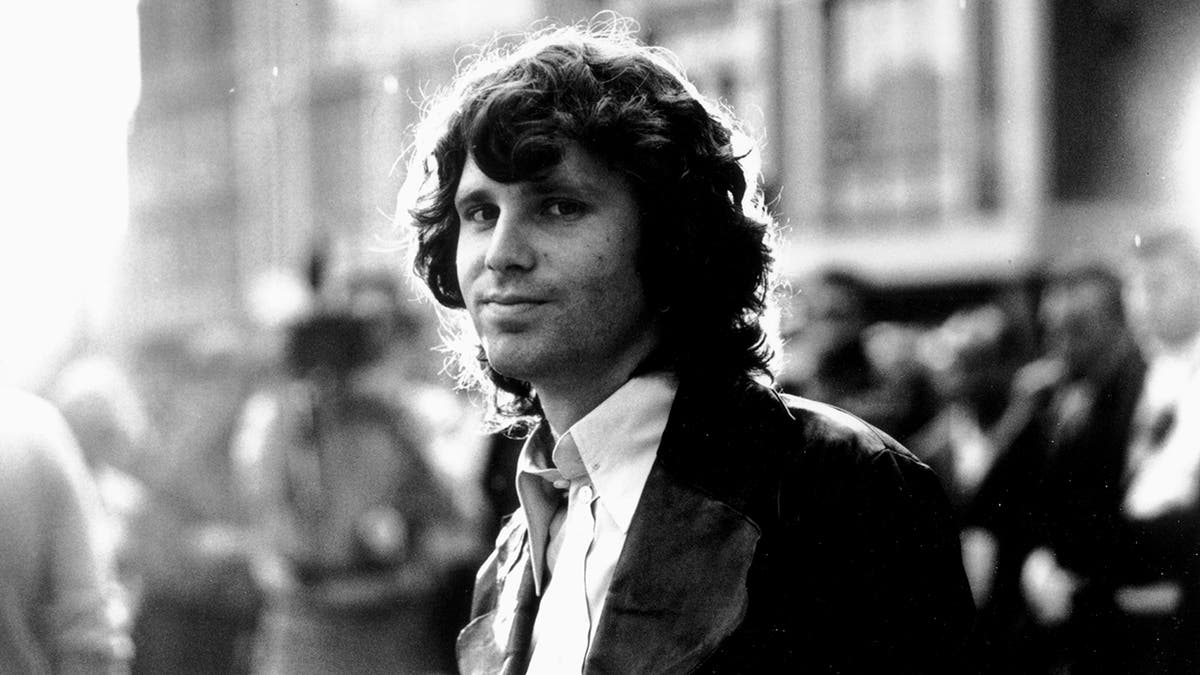 black and white photo of Jim Morrison smirking subtly for the camera