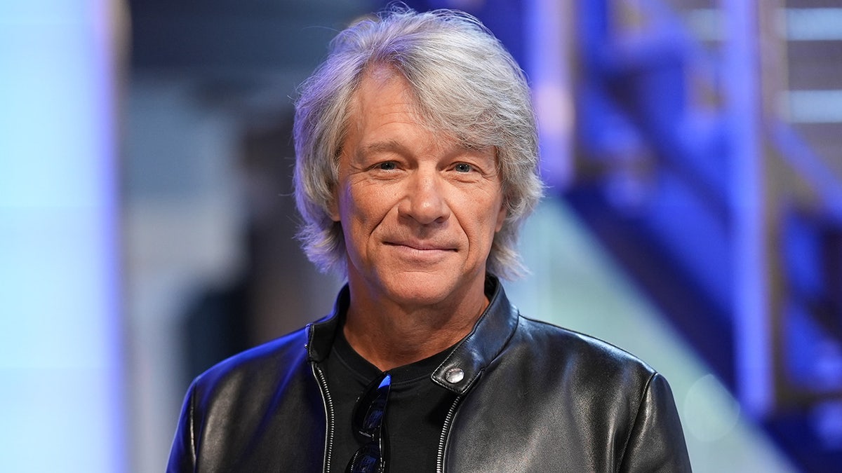 Jon Bon Jovi sorri suavemente e olha diretamente para a câmera vestindo uma jaqueta de couro