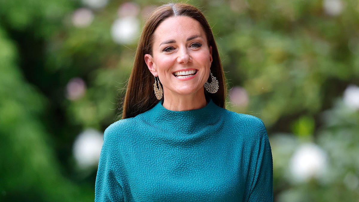 Kate Middleton in a turquoise high neck dress smiles as she walks