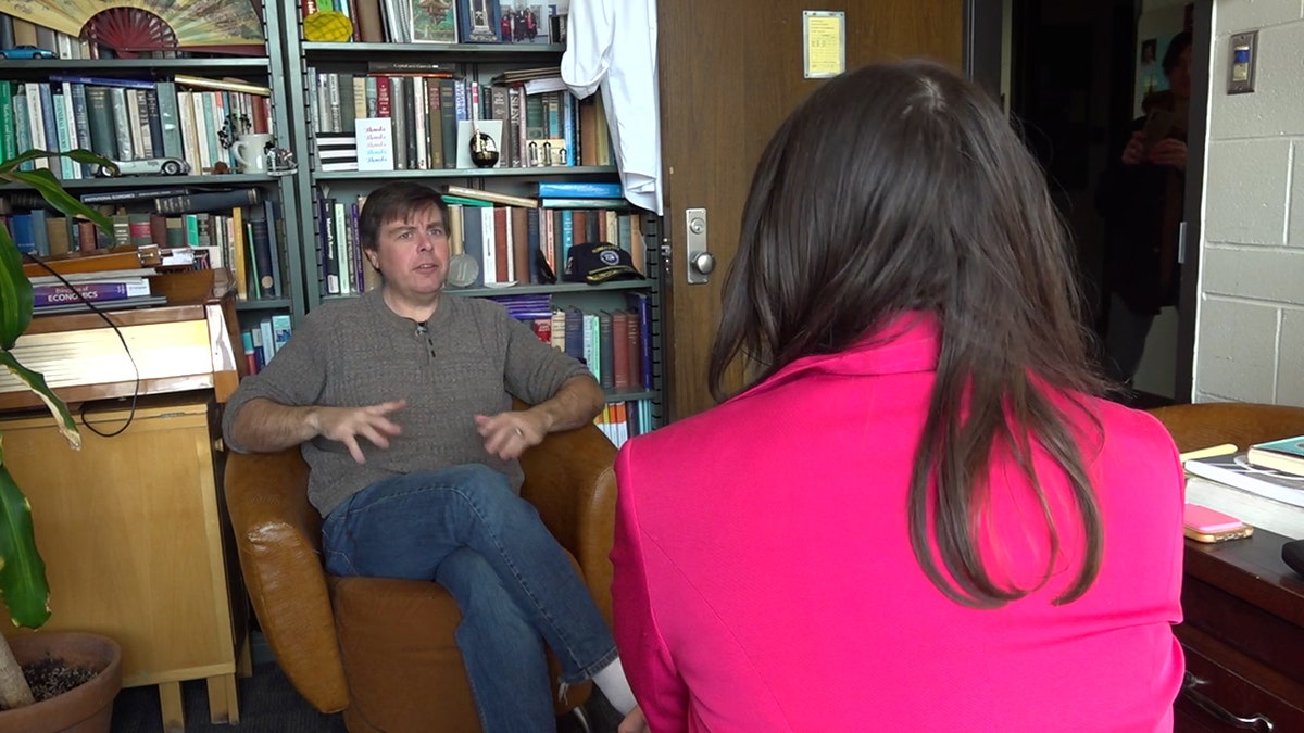 a reporter talks with a professor in front of a wall of books