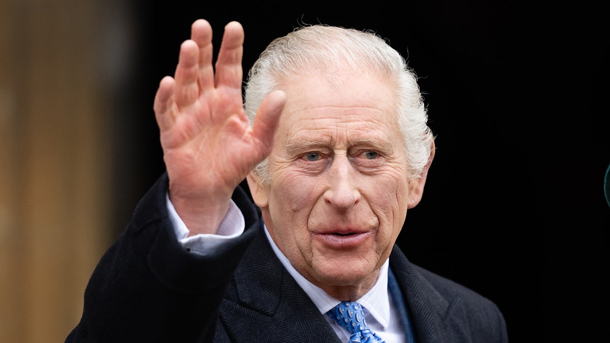 King Charles in a black suit and blue tie waves to the crowd outside Windsor Castle on Easter