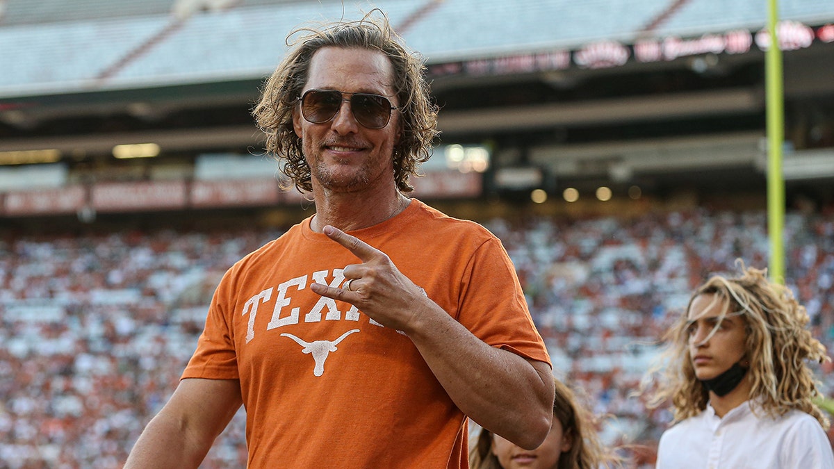 Matthew McConaughey in an orange shirt that says Texas puts up the peace sign