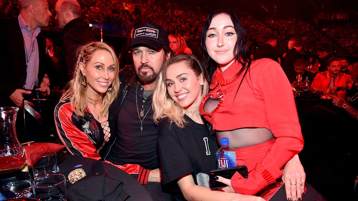 Tish Cyrus puts her arm around Billy Ray Cyrus, who sits next to Miley Cyrus with Noah Cyrus sitting on his lap.