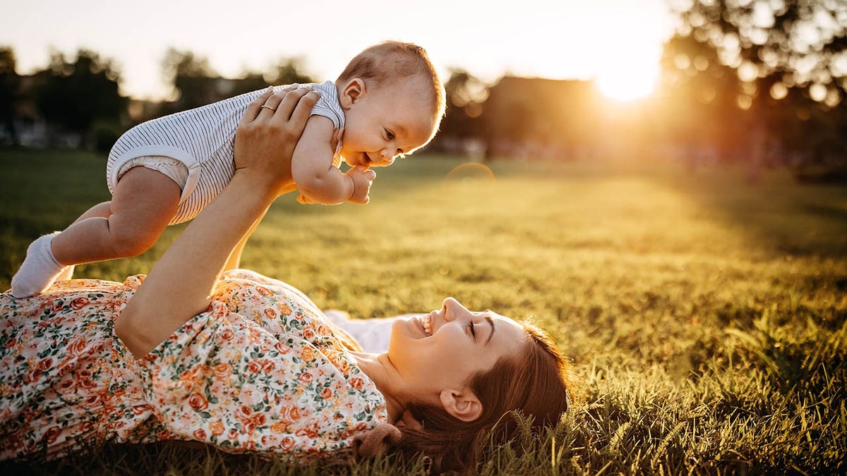 mother laying in grass holding baby