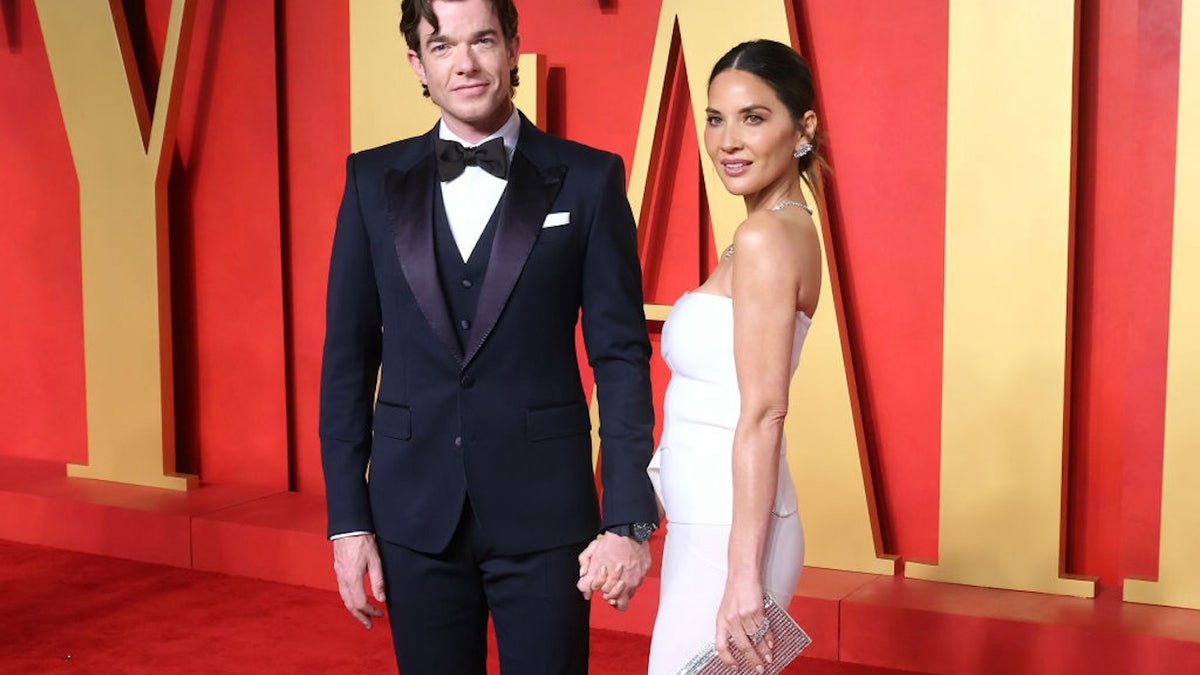 Olivia Munn walks the red carpet wearing a white dress with her partner John Mulaney.