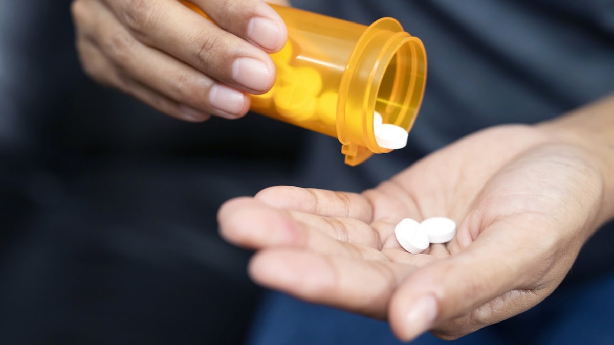 Woman hand with pills on, spilling pills out of bottle on dark background.