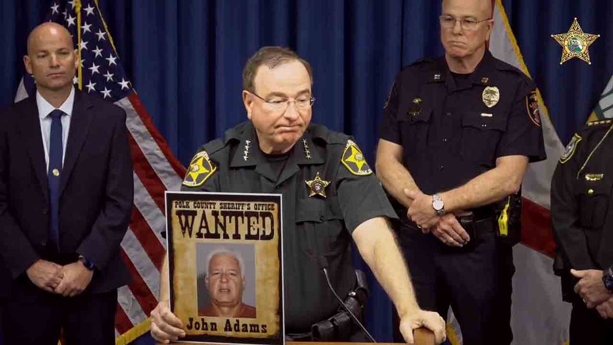 Judd holding photo of man still wanted