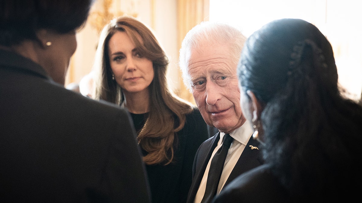 Kate Middleton de preto olha para o rei Carlos III de terno preto e gravata 