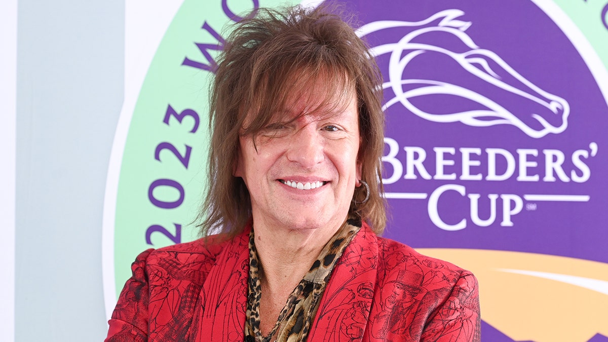 Richie Sambora in a patterned red jacket smiles on the carpet