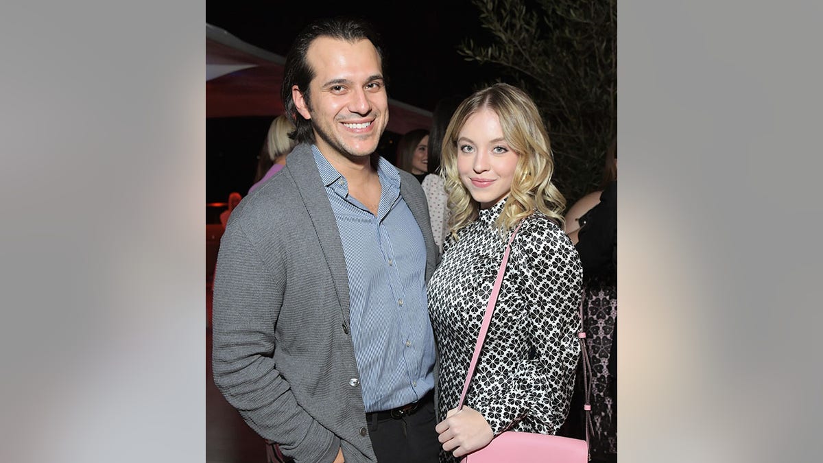 Sydney Sweeney in a printed dress soft smiles with a baby pink purse and Jonathan Davino in a grey sweater and blue button down