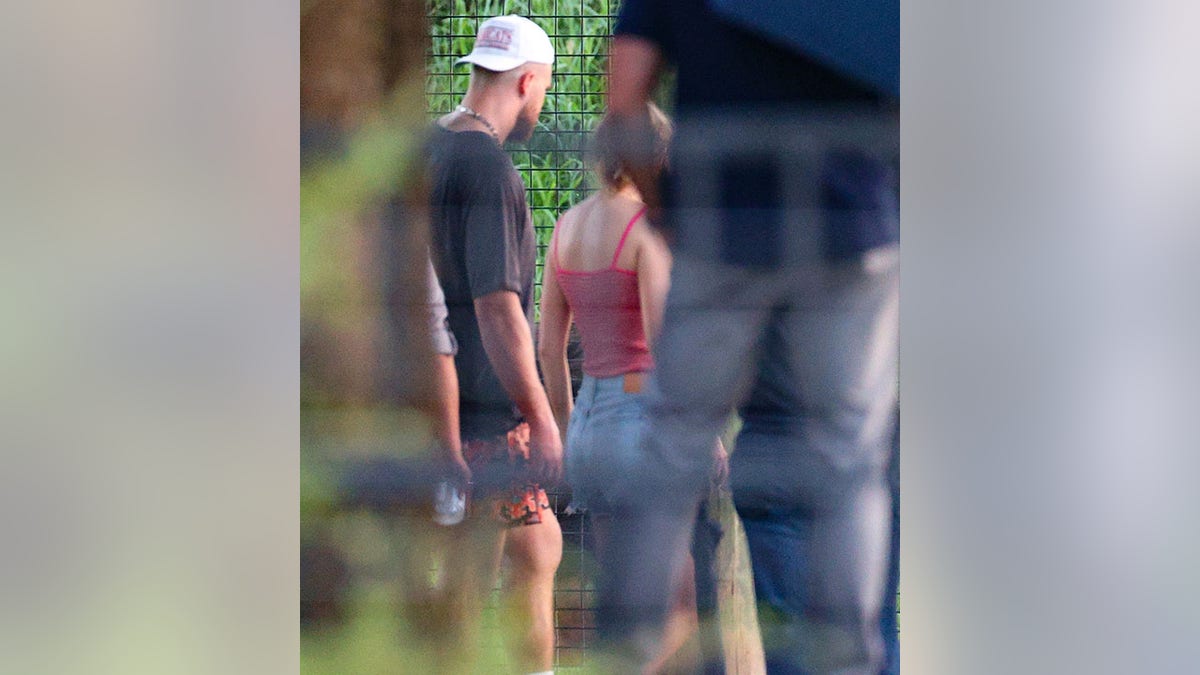 Travis Kelce in a black shirt and backwards baseball cap with Taylor Swift in a red tank top and jeans at the zoo