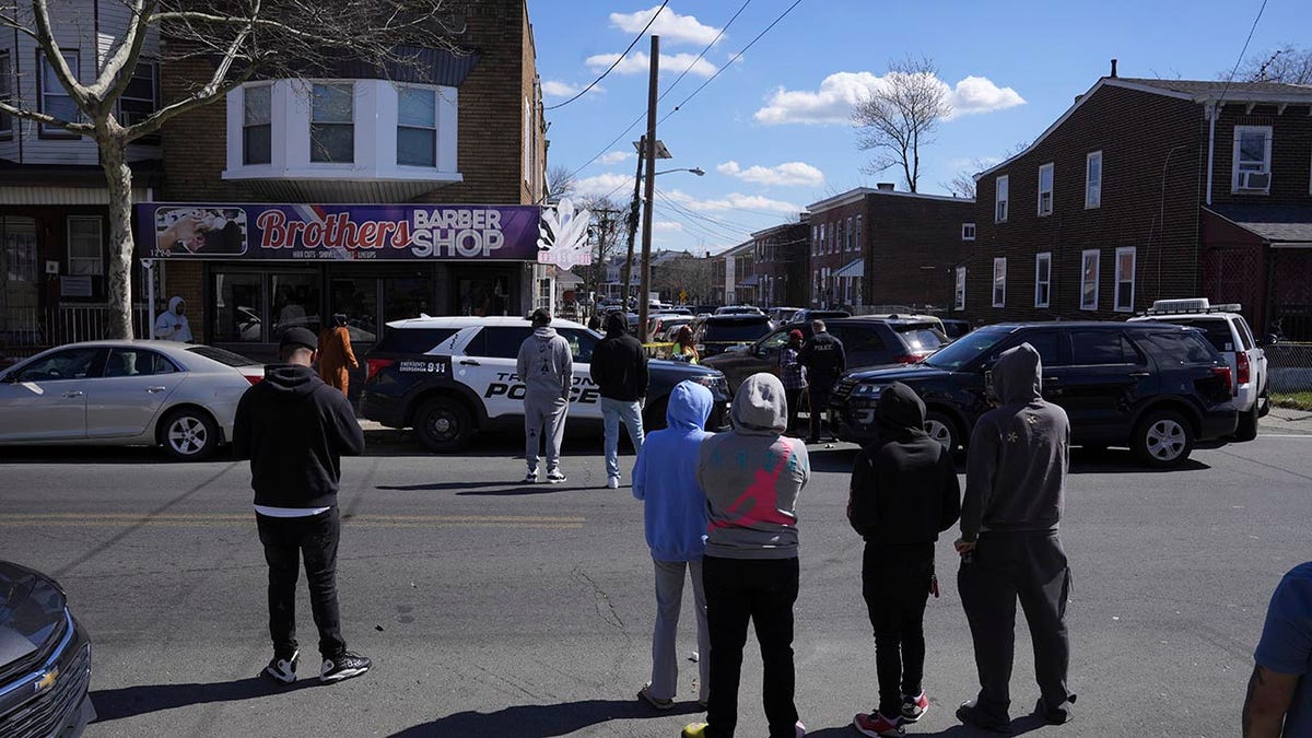 People look on as police surround a home in Trenton, N.J., Saturday. A suspect has barricaded himself in a home after shooting three people to death in suburban Philadelphia.