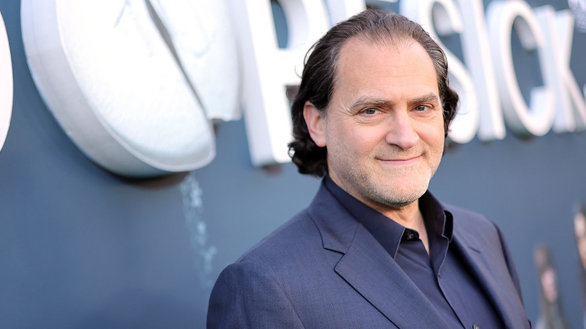 Michael Stuhlbarg in a navy shirt and suit soft smiles on the carpet