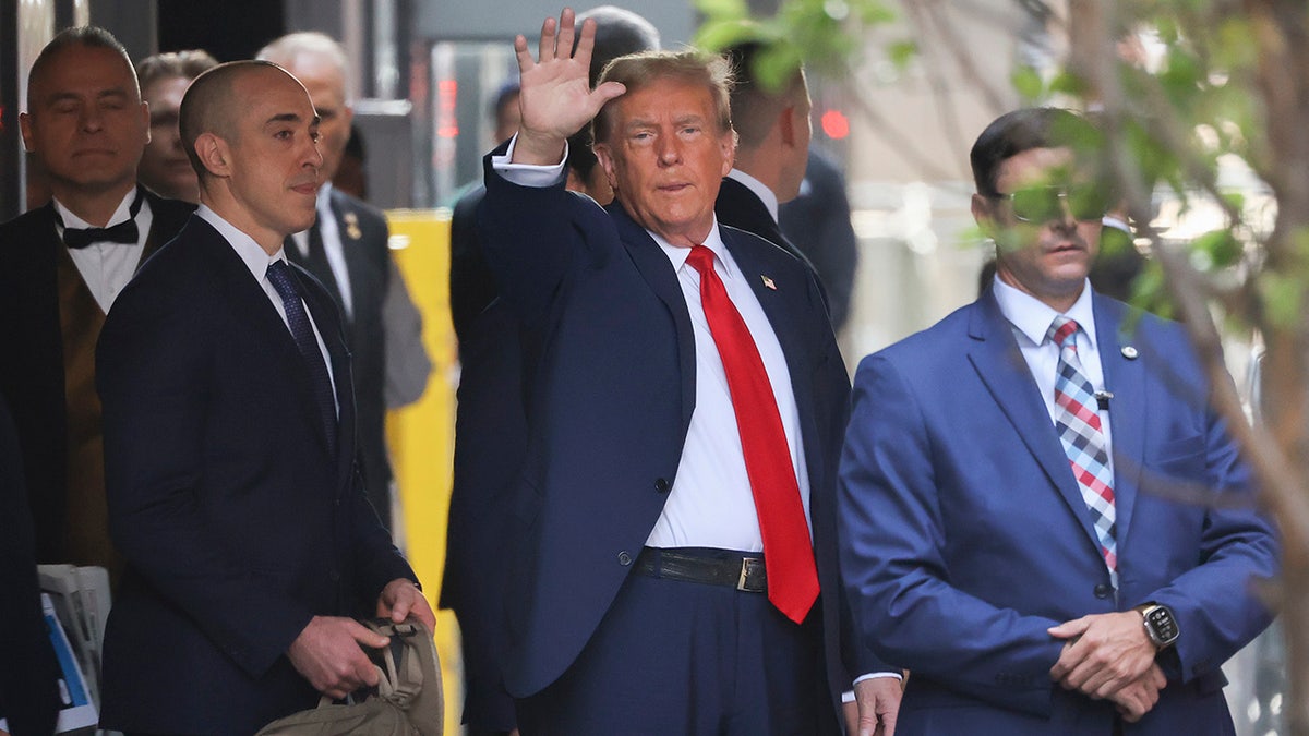 Donald Trump in red tie, white shirt, navy coat waving