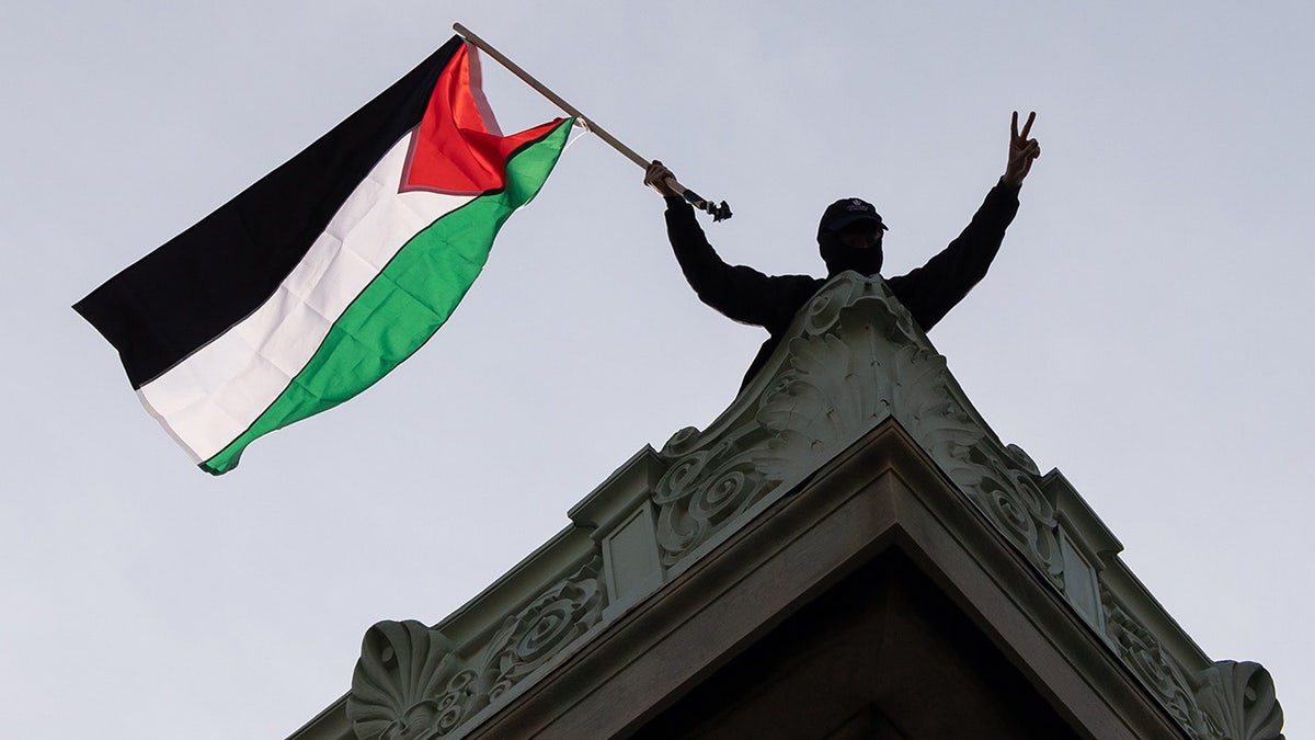 Um manifestante pró-Palestina segura uma bandeira no telhado do Hamilton Hall, na Universidade de Columbia