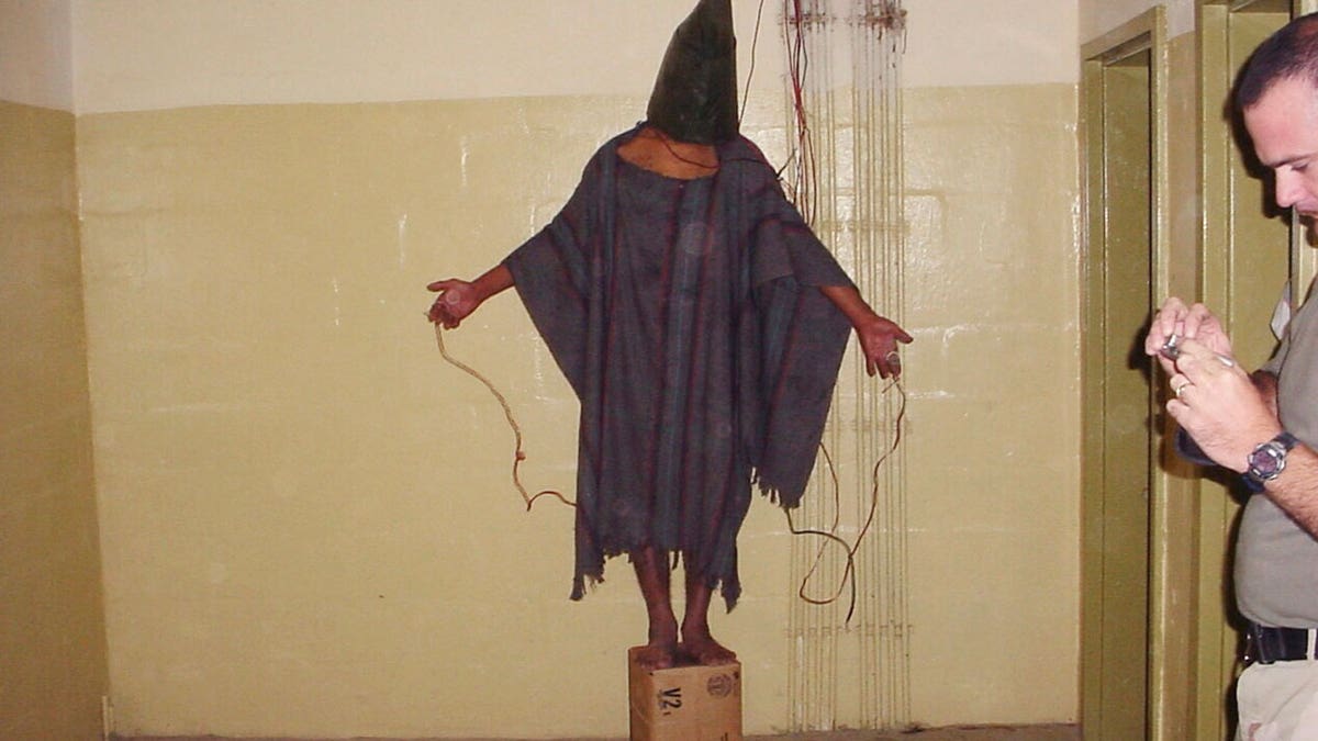 An unidentified detainee standing on a box with a bag on his head and wires attached to him in the Abu Ghraib prison in Baghdad, Iraq.
