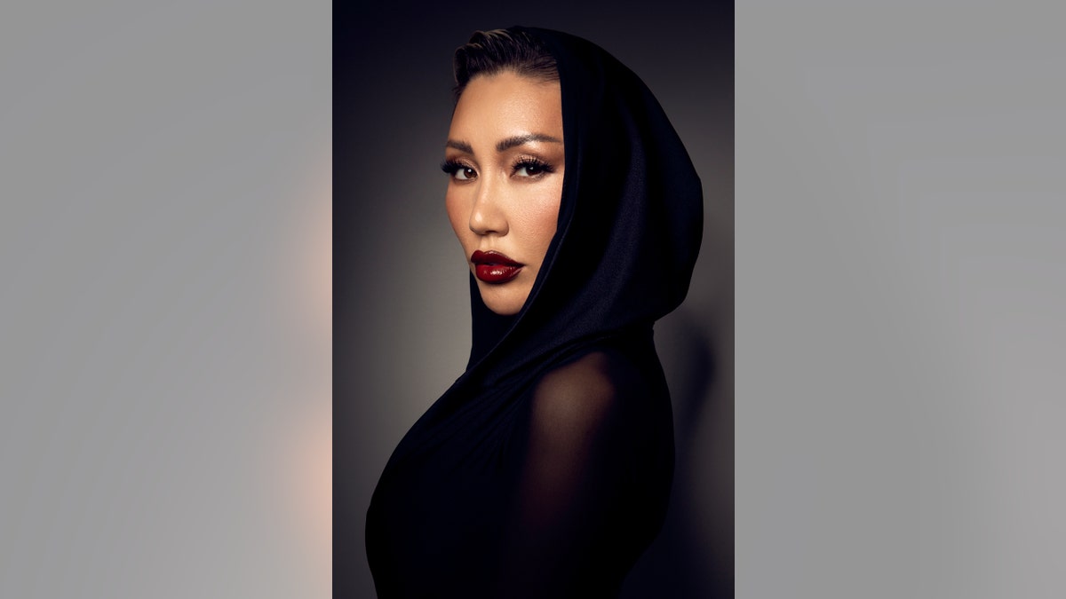 Aliia Roza looking to the side in a sheer black dress and hood