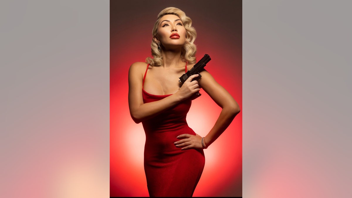 Aliia Roza wearing a red dress and holding a gun