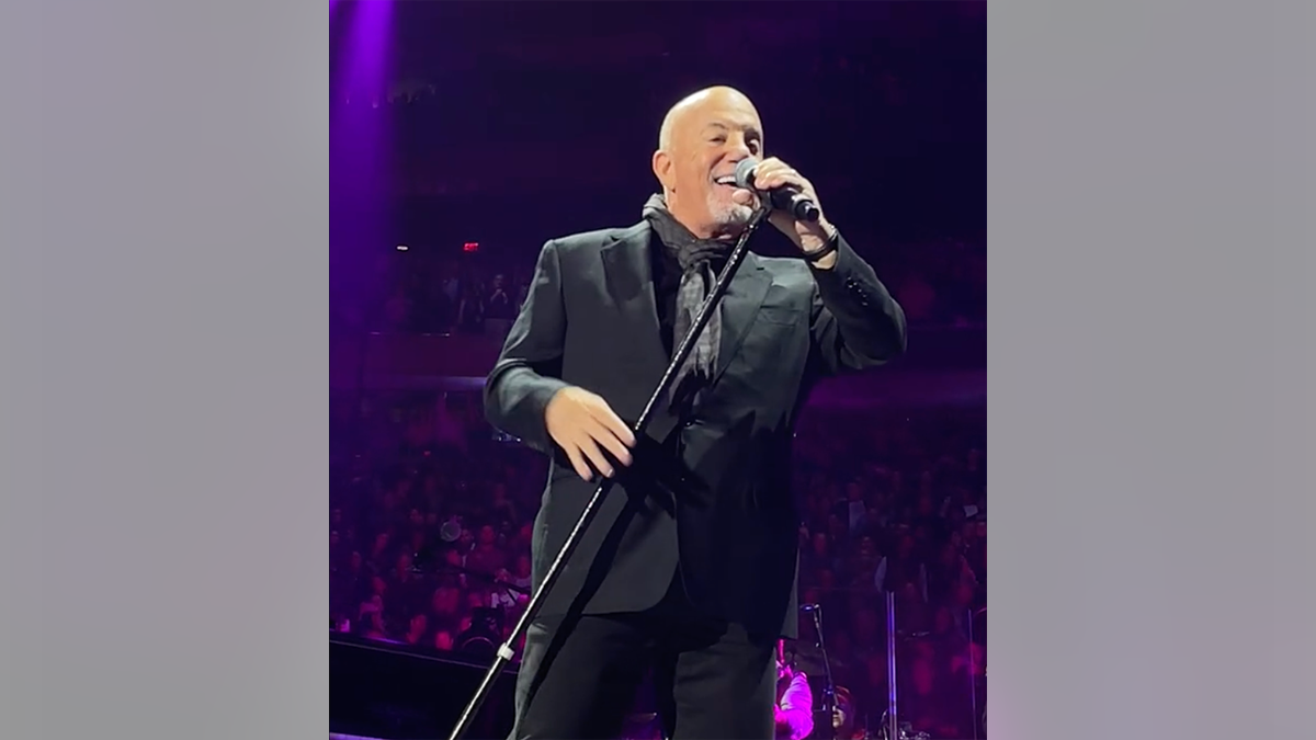 Billy Joel holds his microphone in the air at Madison Square Garden as he performs "Uptown Girl" and smile