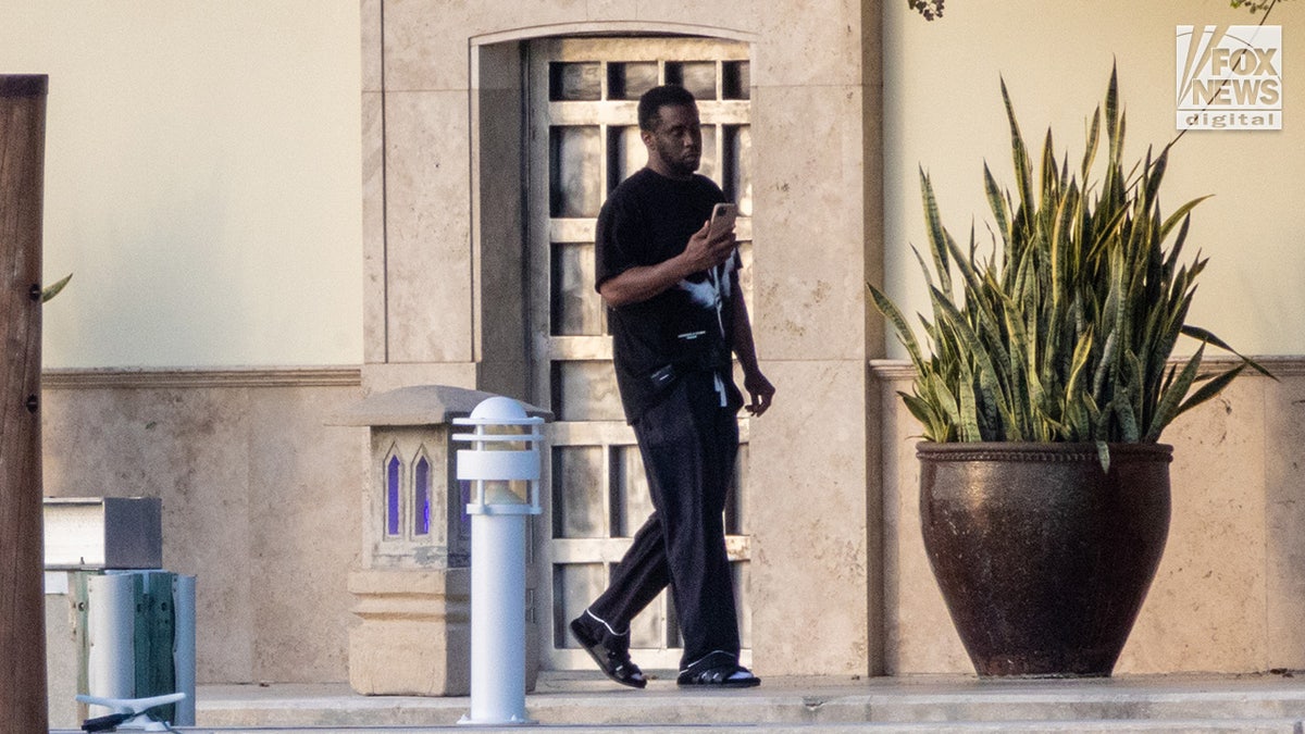 Sean 'Diddy' Combs in all black walks on his dock outside his Miami home looking at his phone