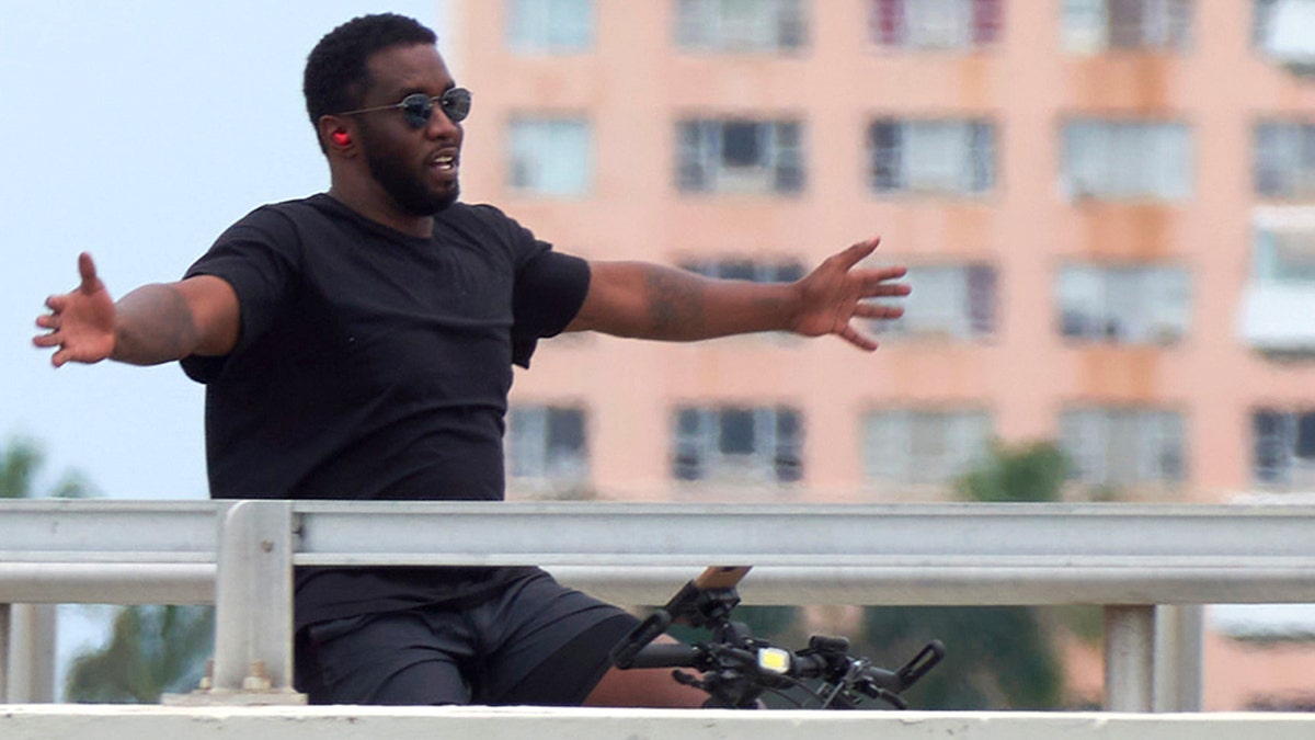 Q Diddy rides a bicycle with his arms outstretched and wears sunglasses.